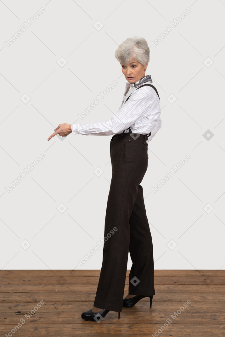 Vue latérale d'une vieille dame en vêtements de bureau pointant vers le bas