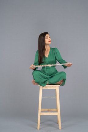 De cuerpo entero de una señorita sosteniendo su clarinete de rodillas mientras está sentada en una silla de madera