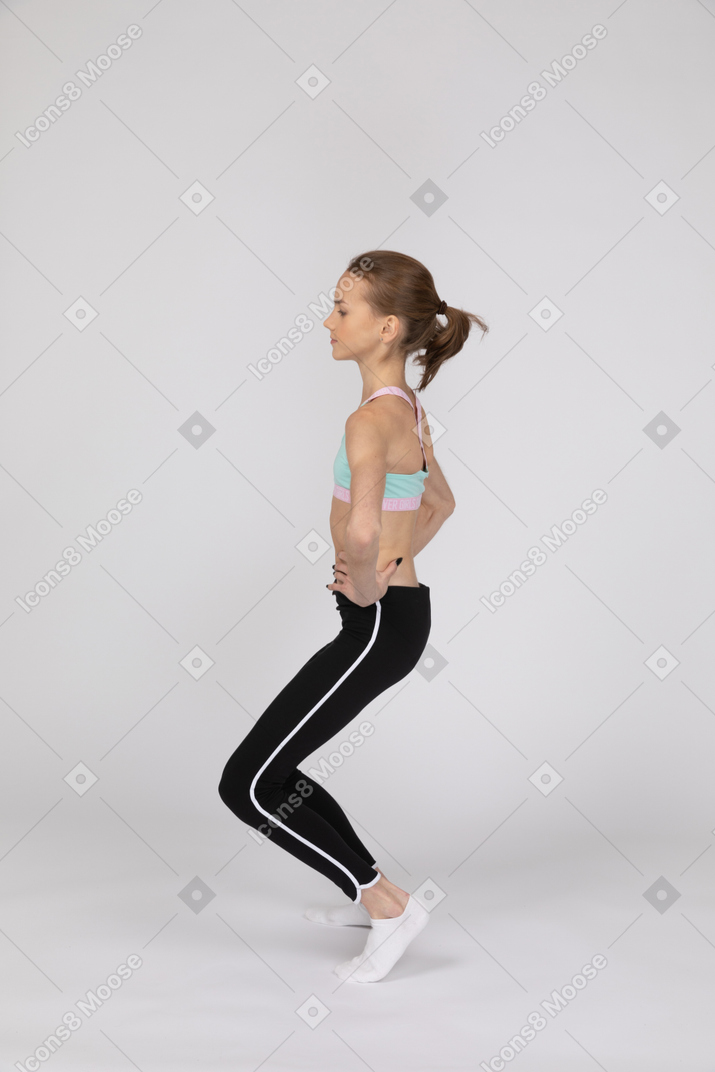 一个十几岁的女孩在运动服把双手哦臀部和弯曲的膝盖的侧视图
