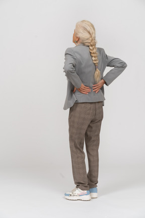 Rear view of an old lady in suit suffering from pain in back