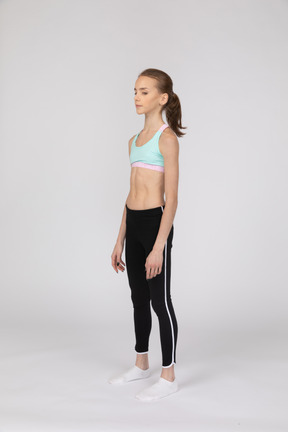 Three-quarter view of a teen girl in sportswear standing still and looking aside
