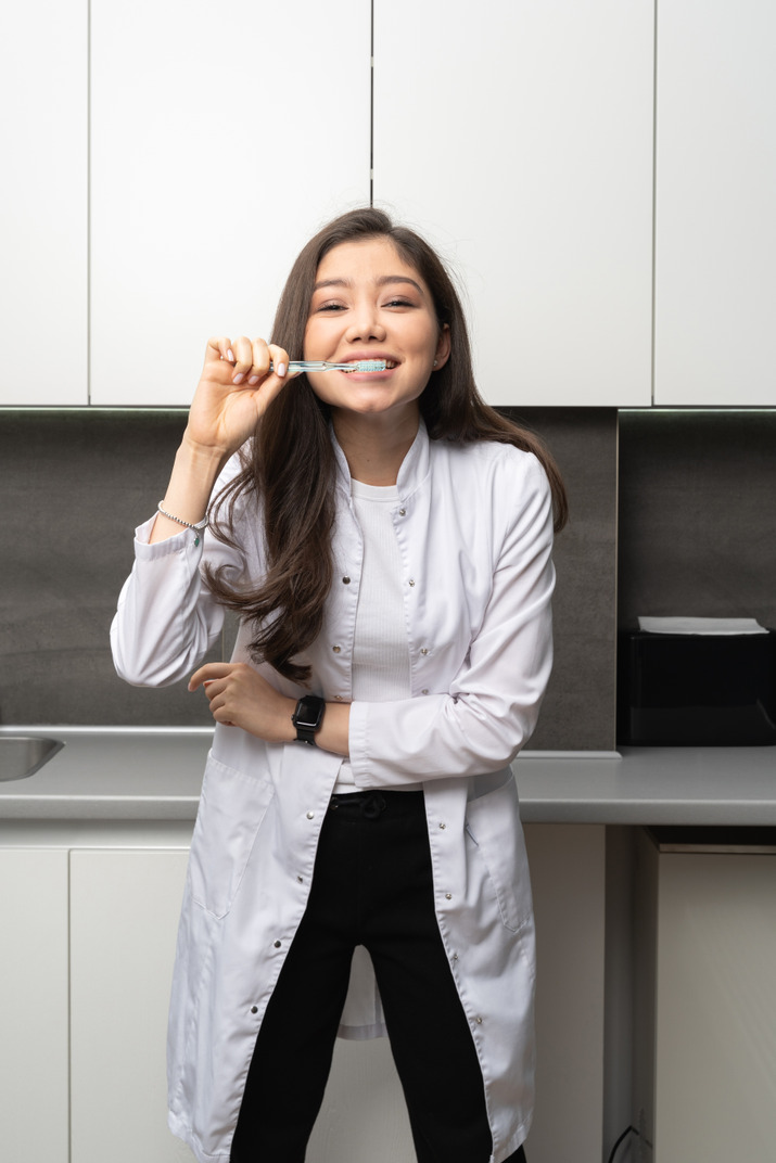Front view of a female dentist brushing her teeth and looking at camera