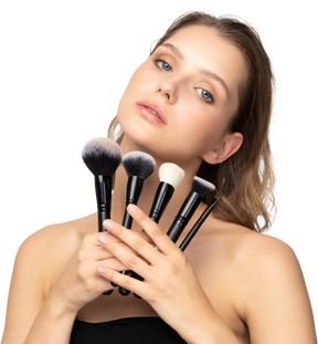 Vue de face d'une jeune femme sensuelle tenant des pinceaux de maquillage et inclinant la tête