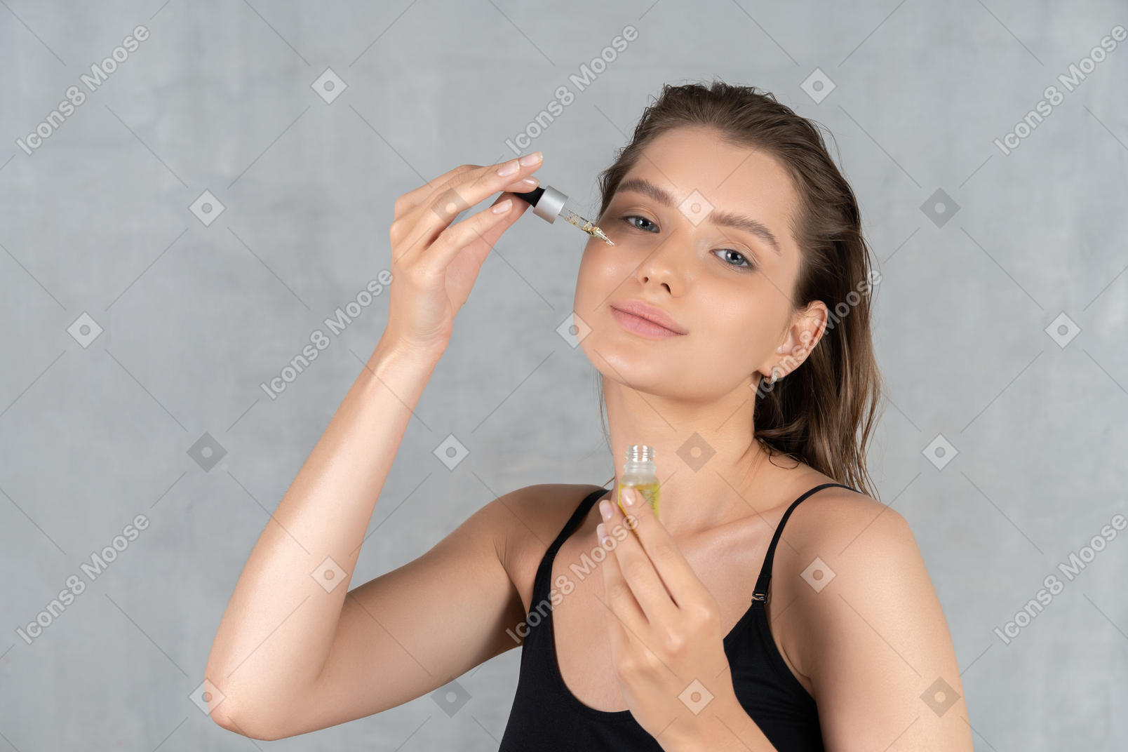 Front view of a young woman smiling while applying face serum