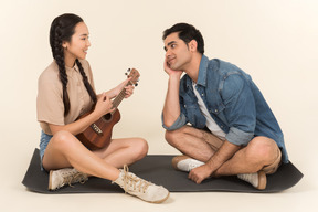 Junge asiatische frau, die ihre gitarre und jungen mann spielt, wird von ihr verzaubert