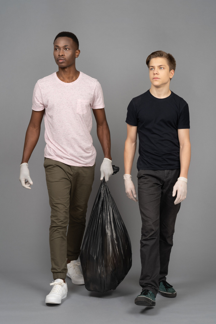 Two young man carrying a trash bag