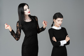 Morticia addams olhando para a quarta-feira que está de pé com as mãos dobradas