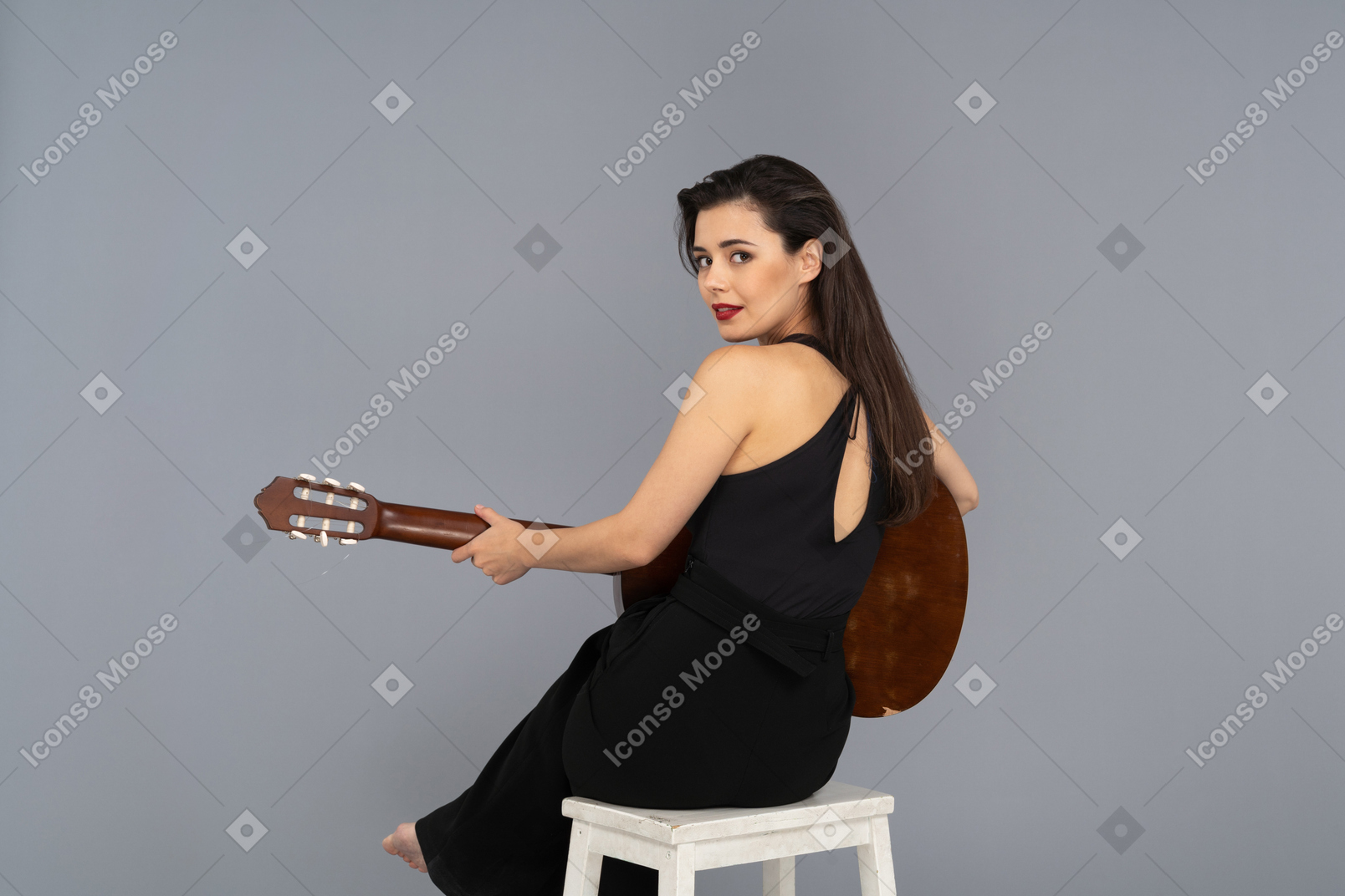 Schöne frau, die eine gitarre spielt, während sie halb sitzt, wandte sich einer kamera zu