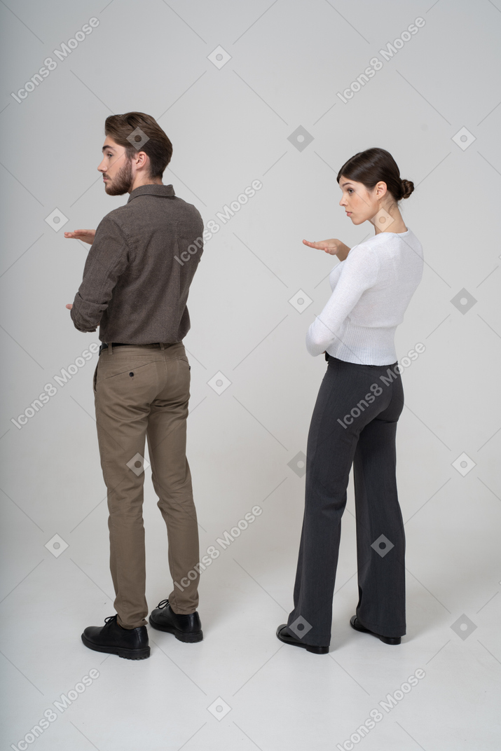 Vue de trois quarts arrière d'un jeune couple en vêtements de bureau montrant la taille de quelque chose