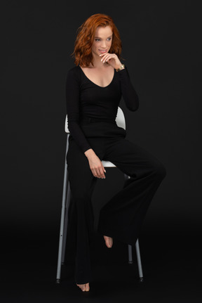 검은 옷을 입고 키가 큰 회색 의자에 앉아 있는 젊은 여성