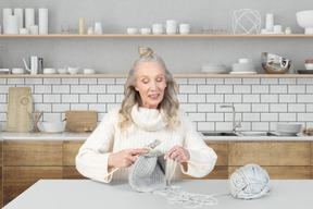 An old woman is knitting in the kitchen