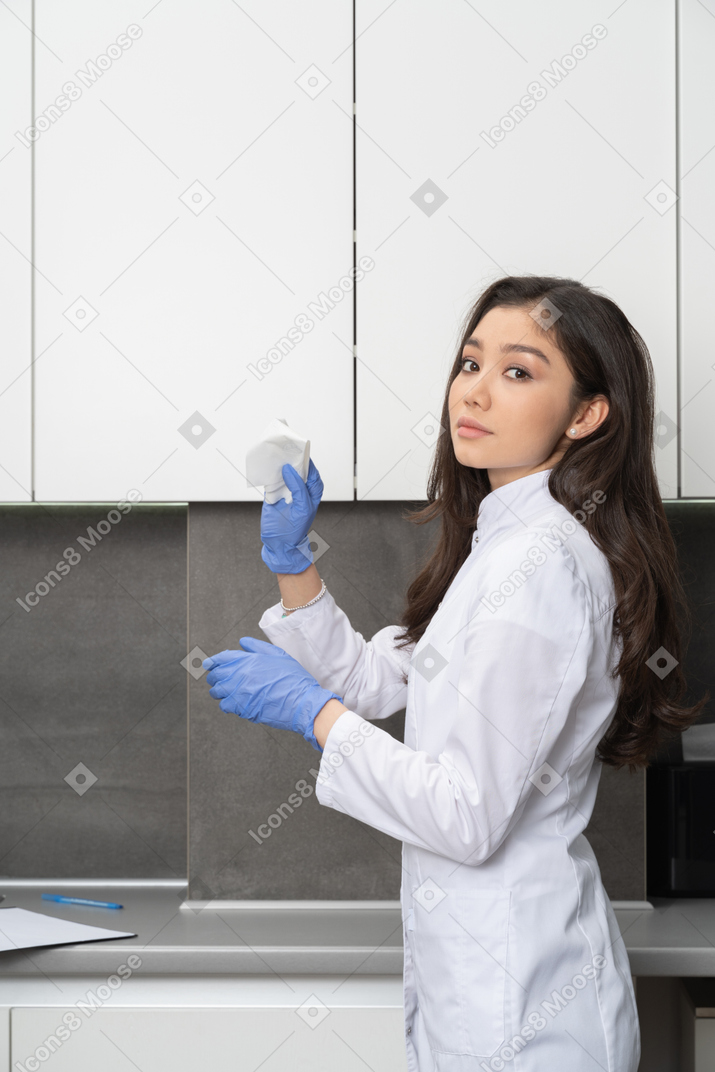 Side view of a female doctor holding a wipe in protective gloves and looking at camera