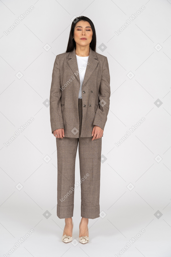 Front view of a young lady in brown business suit standing with her eyes closed