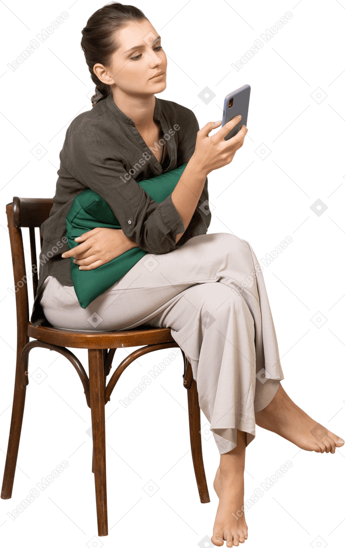 Vorderansicht einer gelangweilten jungen frau, die auf einem stuhl sitzt und ihr telefon überprüft