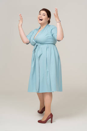 一位身穿蓝色连衣裙、举起双臂摆姿势的快乐女人的前视图