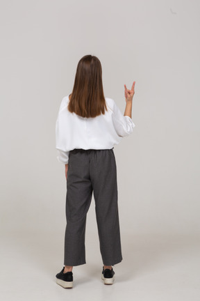 Vue arrière d'une jeune femme en tenue de bureau montrant un geste rock