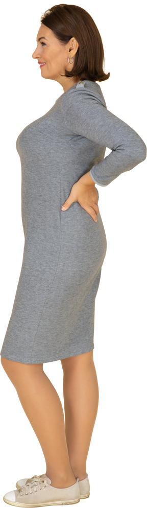Side view of a woman in grey dress standing with hands on hips