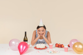Joven mujer asiática sentada frente a pastel de cumpleaños y pidiendo un deseo
