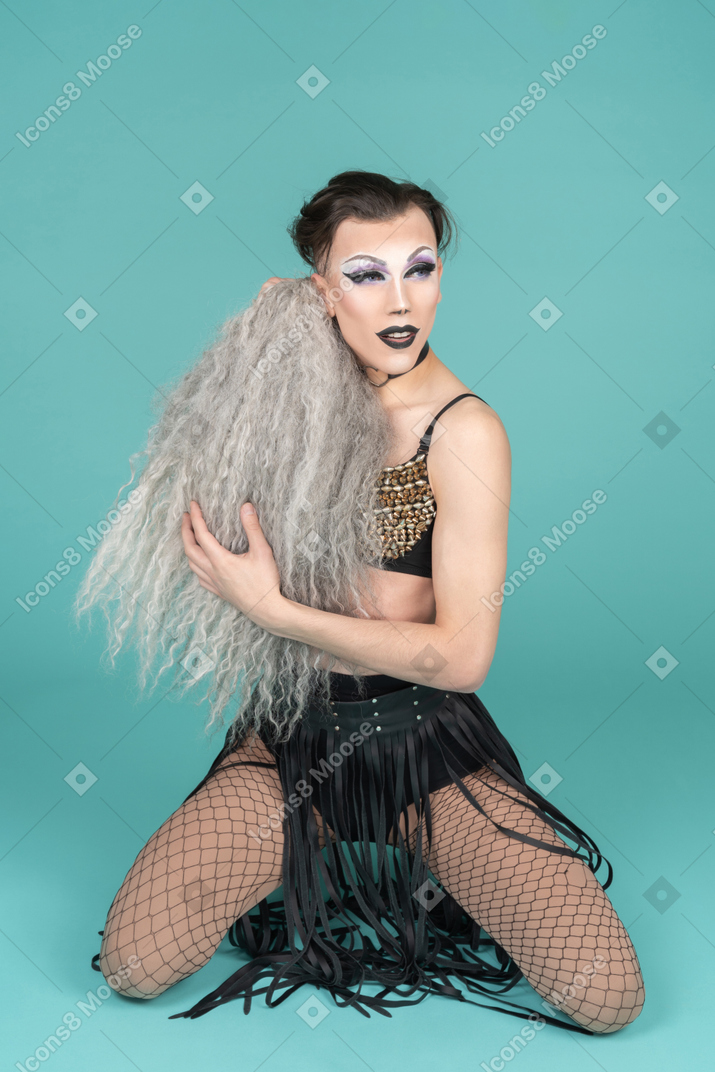 Drag queen standing on knees with gray wig in hands
