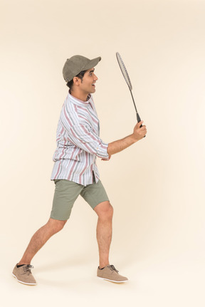 Young caucasian guy standing in profile and holding tennis racket