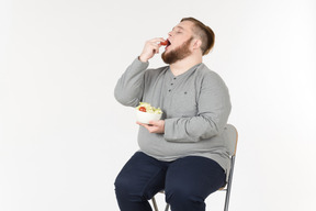 Big bearded man sitting on the chair and eating salad