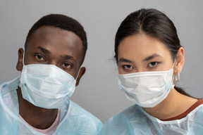 Retrato de duas pessoas com máscaras e roupões médicos
