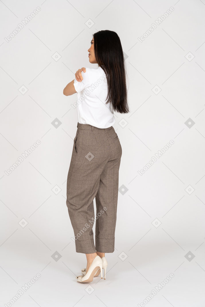 Three-quarter back view of a young lady in breeches and t-shirt embracing herself