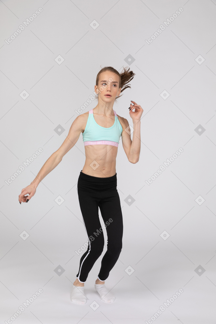 Front view of a teen girl in sportswear raising hand while squatting