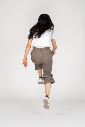 Vista traseira de uma jovem saltitante de calça e camiseta dobrando os joelhos