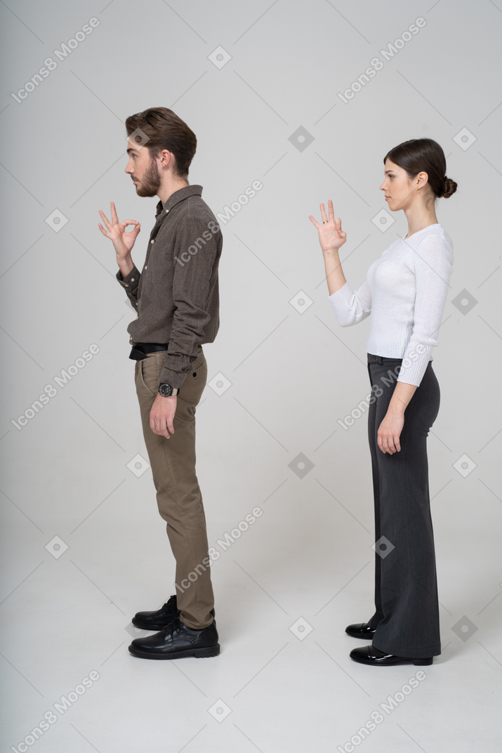 一对年轻夫妇在办公室服装显示ok的手势的侧视图