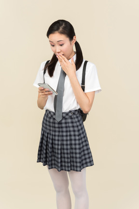 Asian school girl gasping while using smartphone