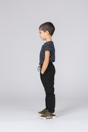 Vue latérale d'un garçon mignon dans des vêtements décontractés posant avec les mains dans les poches
