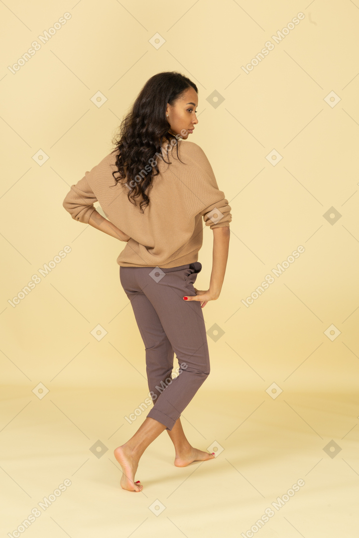 Three-quarter back view of a dark-skinned young female putting hand on hip