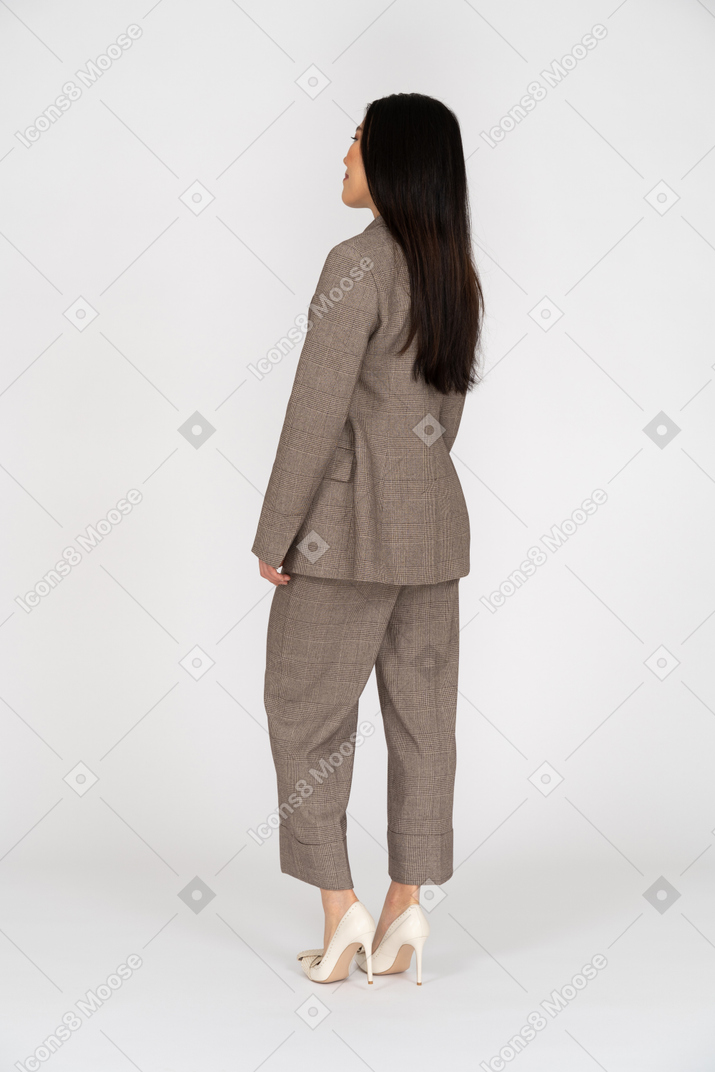 Three-quarter back view of a pleased smiling young lady in brown business suit