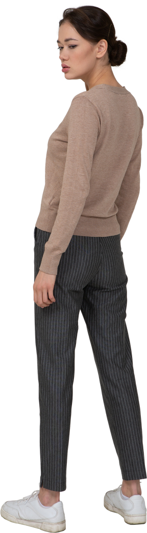Vista posterior de tres cuartos de una señorita malhumorada inmóvil en suéter y pantalones mirando a un lado