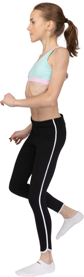 Vista lateral de uma adolescente em roupas esportivas inclinando os ombros e levantando a perna