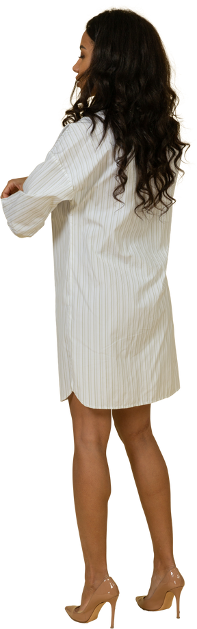Vista posteriore di tre quarti di una giovane donna dalla carnagione scura in abito bianco che si rimbocca le maniche