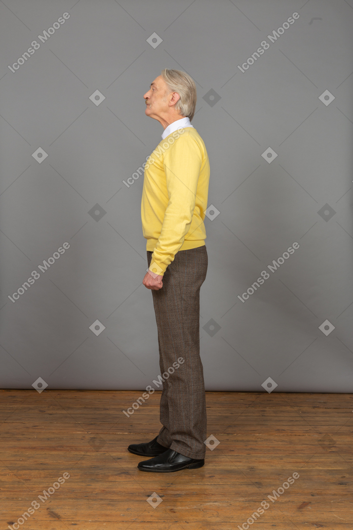Side view of an old curious man in yellow pullover raising head and looking aside