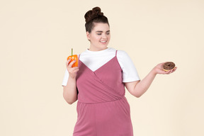 Young plus size woman in a fuchsia jumpsuit posing with food against a pastel yellow background