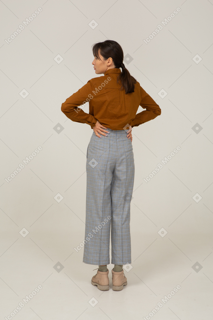一位身着马裤和衬衫的年轻亚洲女性把手放在臀部的后视图