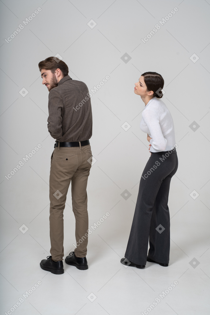 一对穿着办公室服装的年轻夫妇摸着肚子的四分之三后视图