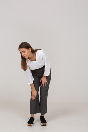 Vista frontal de uma jovem com roupas de escritório, curvando-se e tocando o joelho