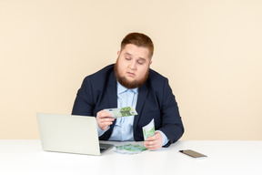 Young overweight office worker sitting at the desk and counting money