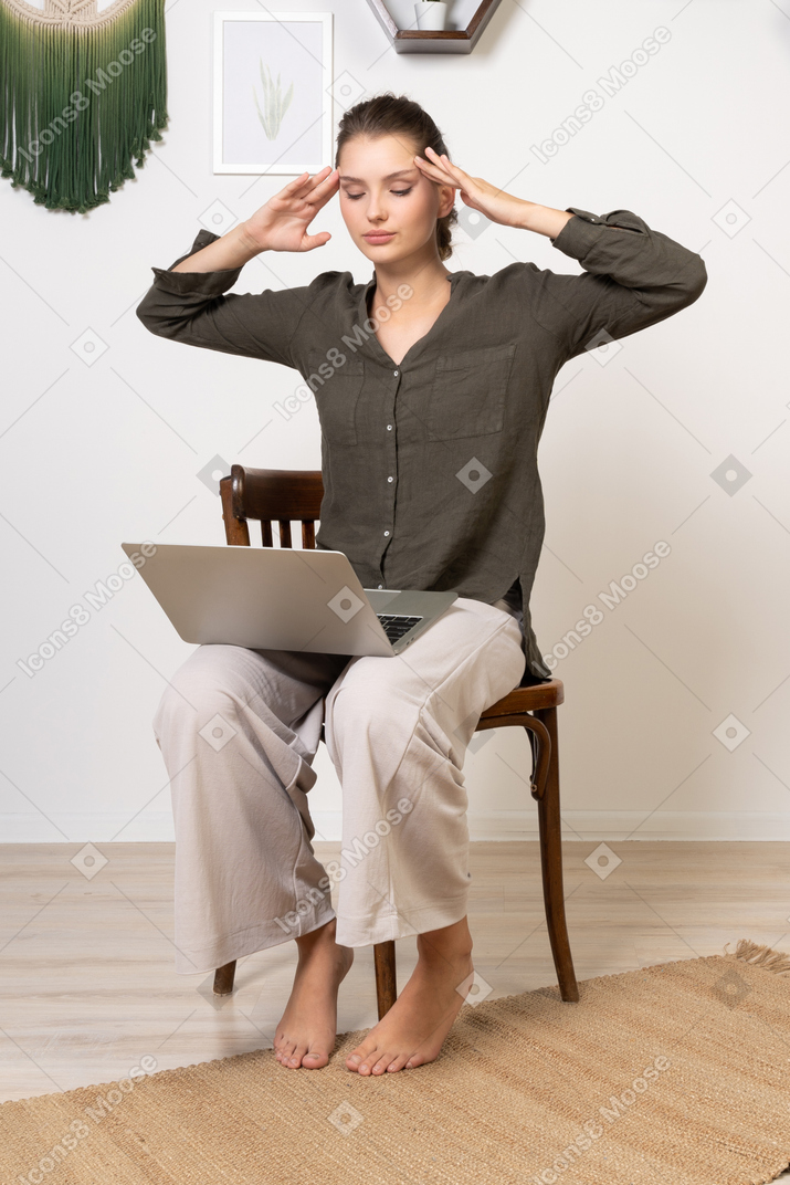 Three-quarter view of a busy young woman with a headache sitting on a chair with a laptop