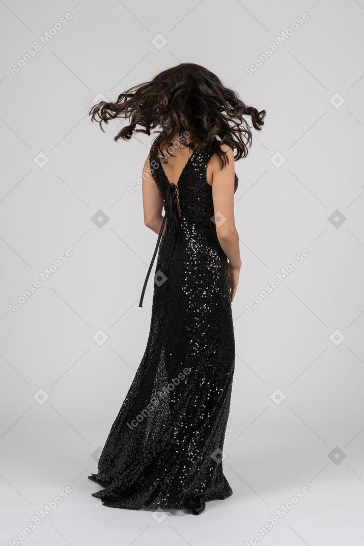 Donna in abito da sera nero in piedi di nuovo alla telecamera e scuotendo i capelli