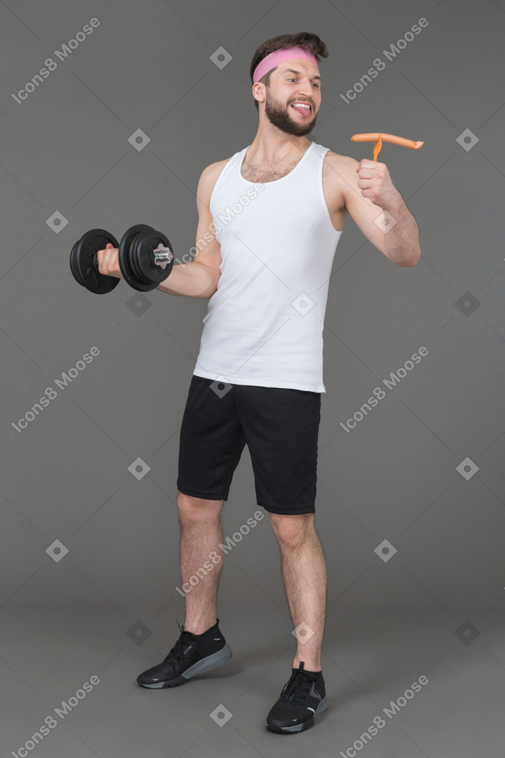 Cheerful man with a dumbbell looking with love at a sausage in his hand