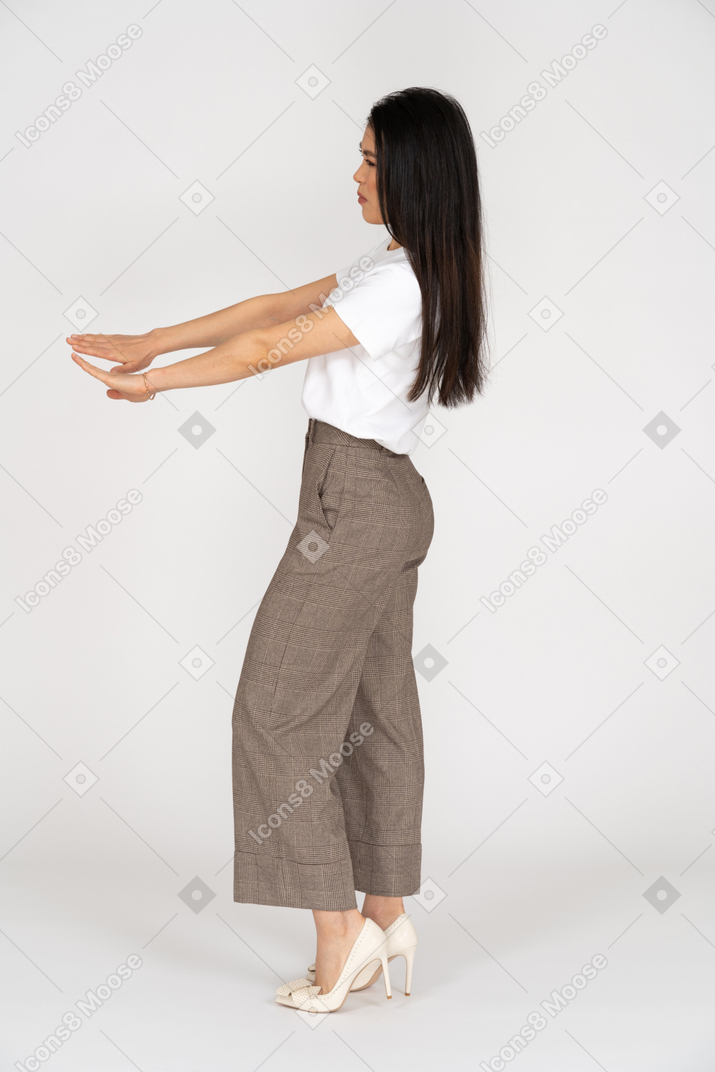 Vista lateral de uma jovem de calça esticando as mãos