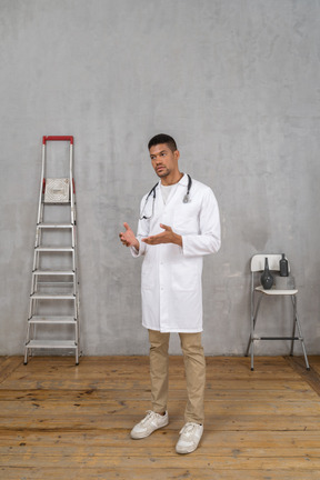 Three-quarter view of a young doctor standing in a room with ladder and chair explaining something