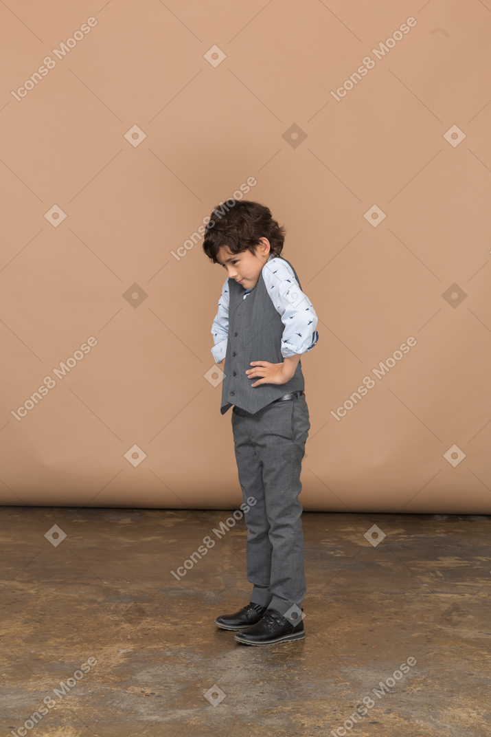 Vista laterale di un ragazzo in abito grigio in piedi con le mani sui fianchi e guardando in basso