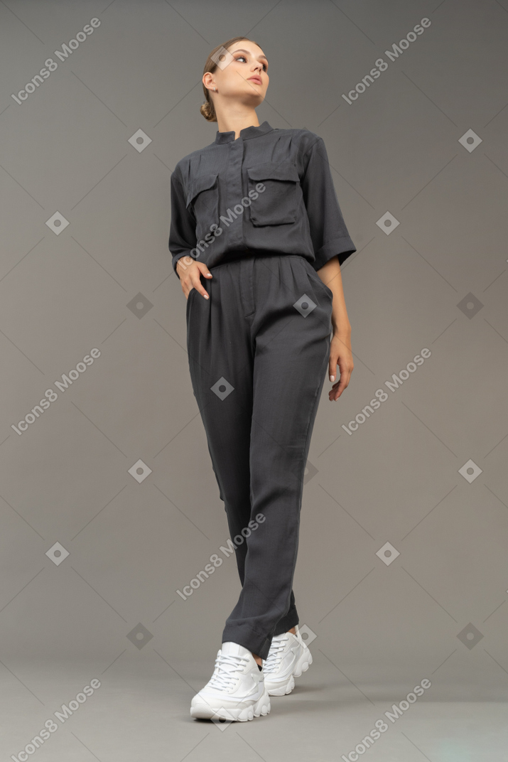 Front view of a walking young woman in a jumpsuit holding hand in pocket